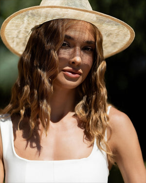 Model in white Norivelle dress with straw accessory