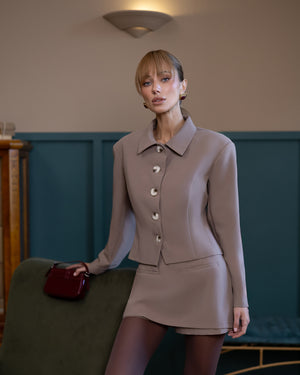 Woman in a beige suit holding a red handbag in an indoor setting.
