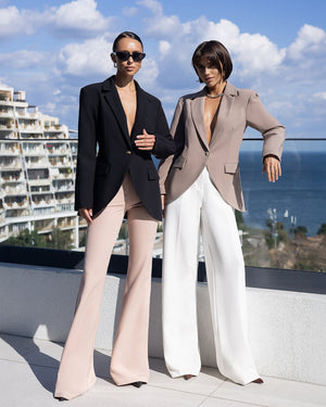 Two women in stylish outfits standing on a rooftop with ocean view