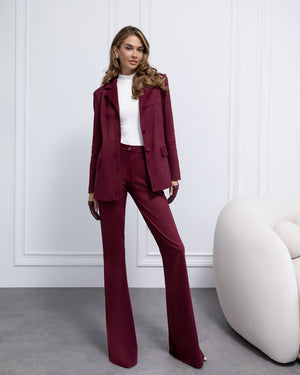 Woman wearing a burgundy suit with a white wall and modern chair in the background