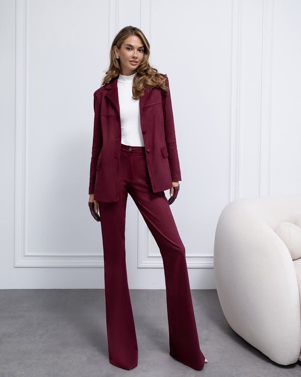 Woman wearing a burgundy suit with a white wall and modern chair in the background