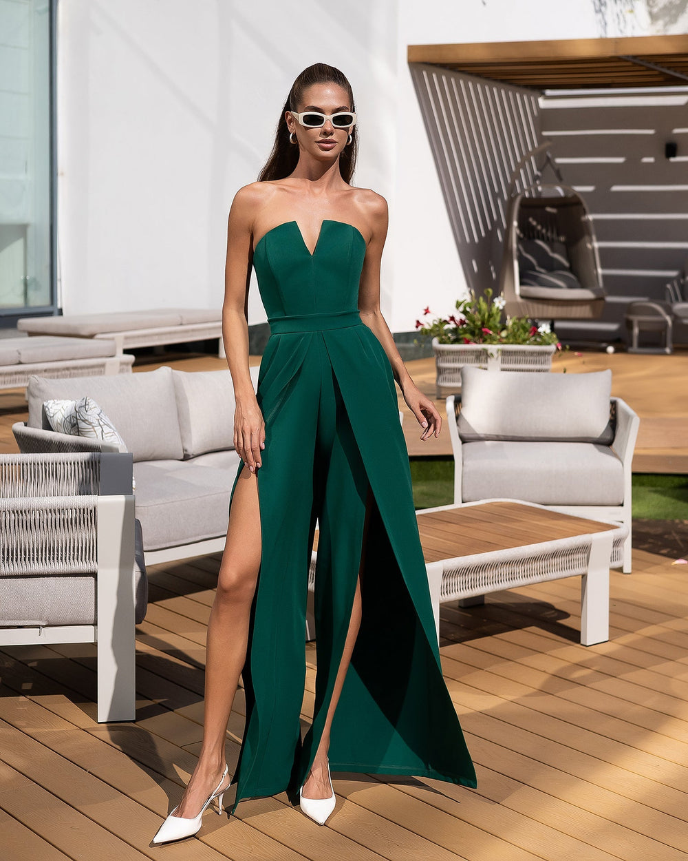 Woman in a green strapless dress with a high slit standing on a wooden deck.